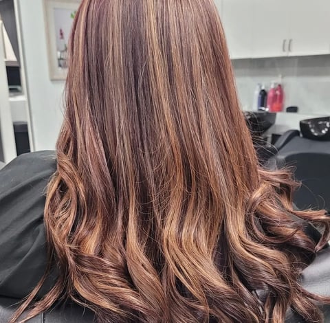 Back view of woman with long, layered hair featuring warm brown tones and copper highlights