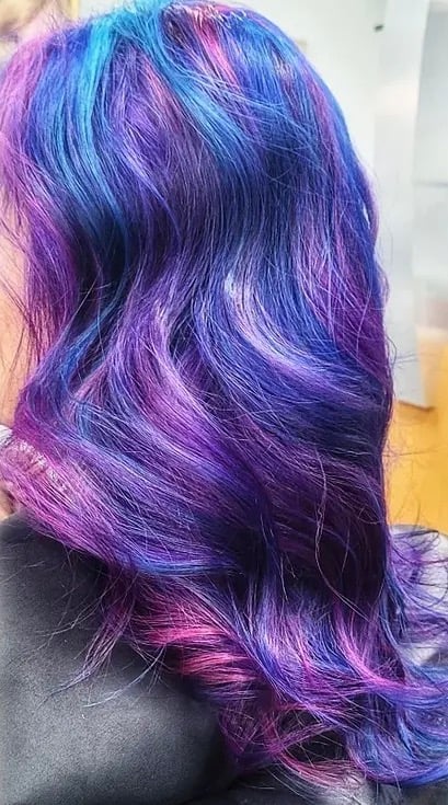 Person with long wavy hair dyed in vibrant purple, blue, and pink ombre colors