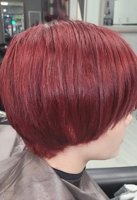 Back view of person with short burgundy red bob haircut in a hair salon setting
