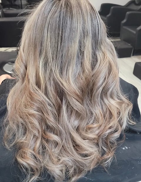Back view of woman with long platinum blonde and beige toned wavy hair in a salon setting