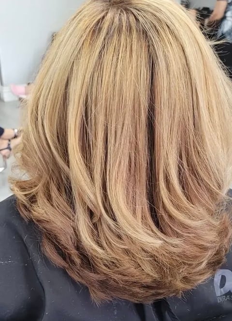 Back view of a woman with shoulder-length layered blonde hair featuring warm highlights and soft waves