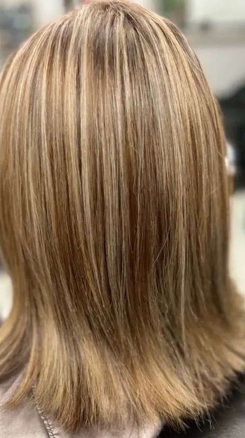 Back view of a woman with long, straight layered blonde hair with darker roots and highlights