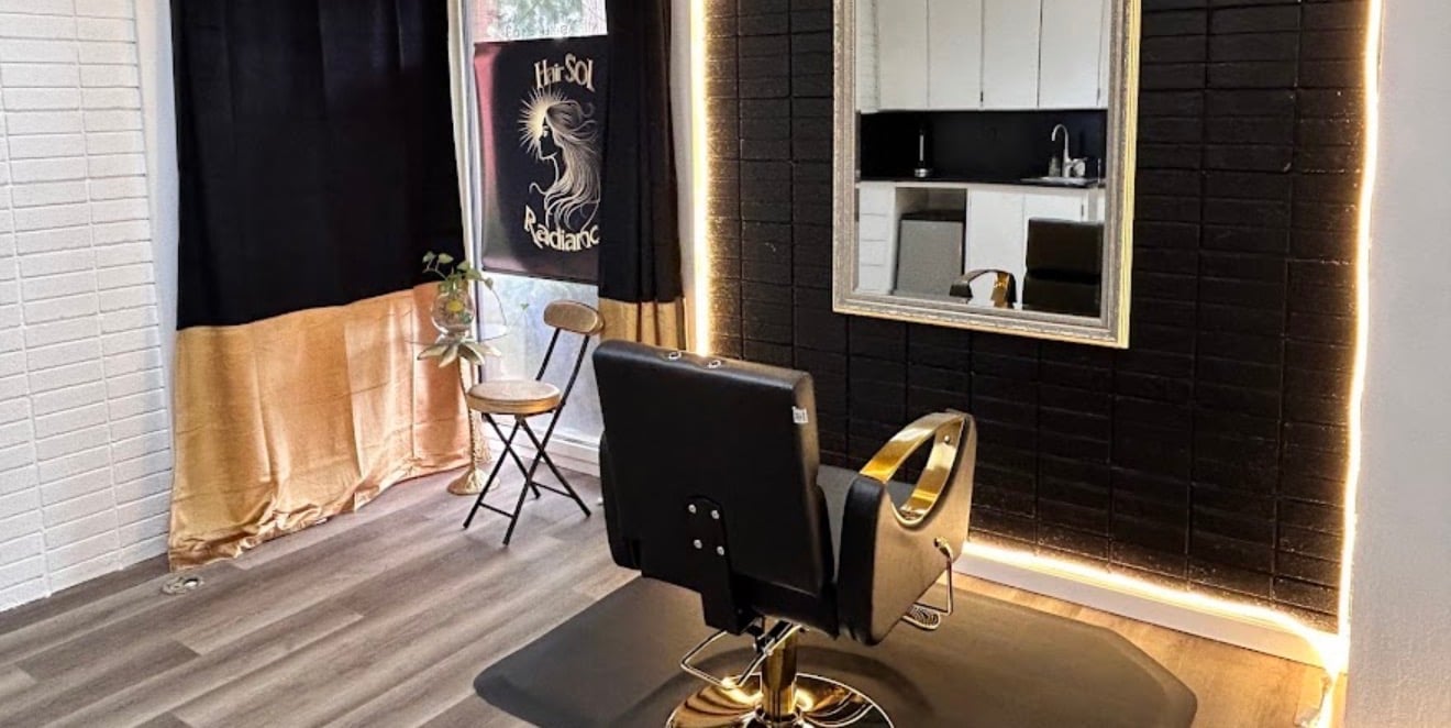 Modern salon chair in front of large mirror with gold accents, black cabinetry, and ambient lighting