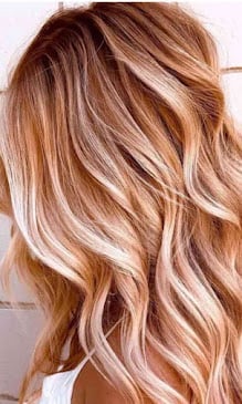 Woman with long wavy hair featuring honey blonde and rose gold highlights with a tousled beachy waves style