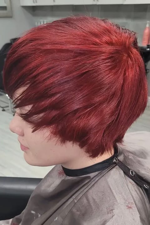 Side profile of person with short burgundy red pixie haircut in a salon setting