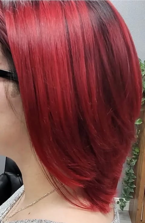 Back view of a person with shoulder-length, vibrant red dyed hair with dark roots