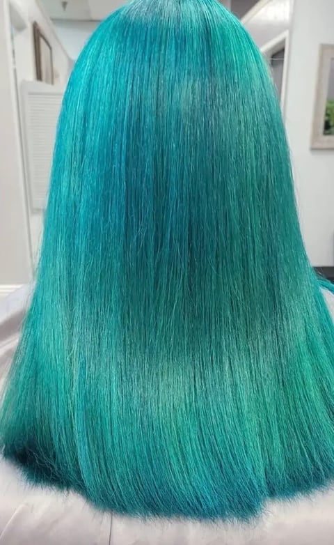 Back view of a person with long, straight turquoise-colored hair styled in a blunt cut